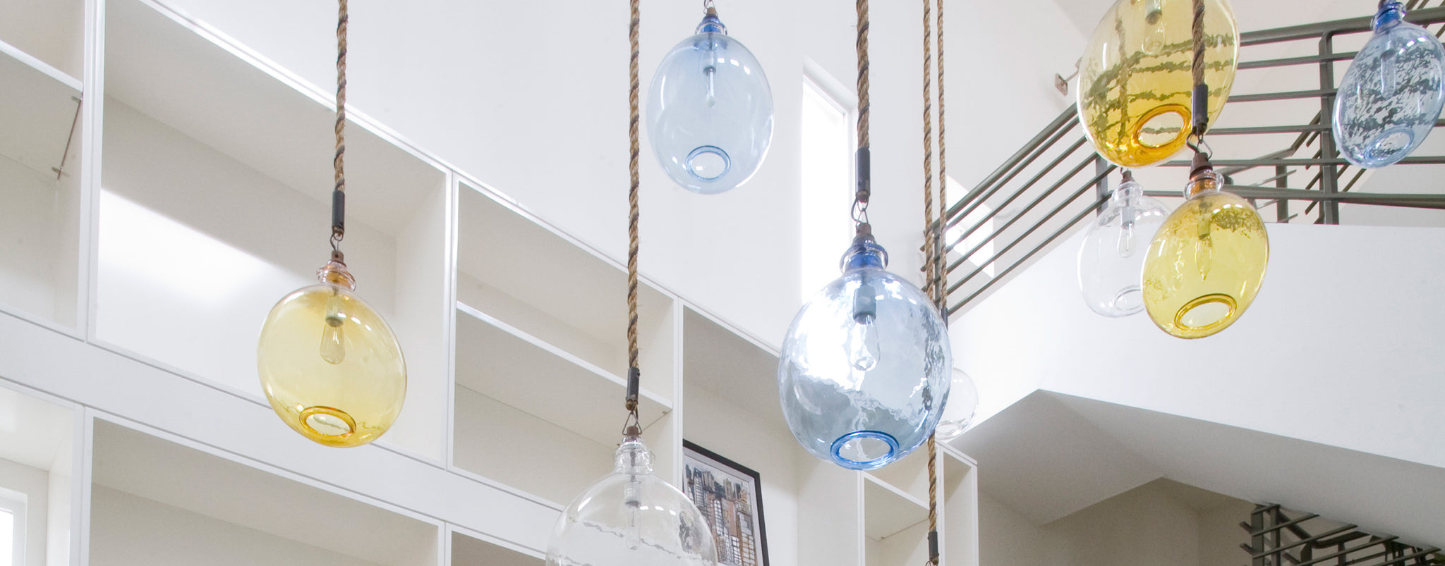 hanging pendent glass lights in yellow, blue and clear in a bright interior with white architectural details and a stairway to the right