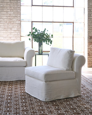  White chair on a brown rug next to a white sofa and side table with a plant on top. Photographed in Brevard Ivory. 