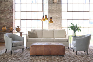  White sofa in a showroom with 3 glass light pendants, 2 grey leather chairs on the side and a brown ottoman in front. Photographed in Lester Snow.. 