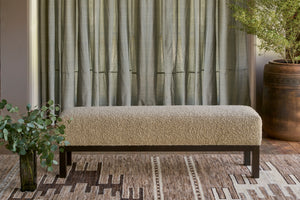  Bench with a wood base with a vase with foliage in front, on a brown rug with a design. Curtains in the background. Photographed in Knobby Mineral. 