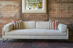  Sofa in front of a wood wall with a square mirror. Two striped pillows on the sofa. Photographed in Andrews Natural. 