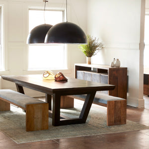  Dining room photo. Rectangular dining table with two upholstered benches on either side as seating. There are two black circular pendants hanging above dining table. The dining set is placed in a white room with a large window, the wall adjacent to the window has a wood credenza against it.  