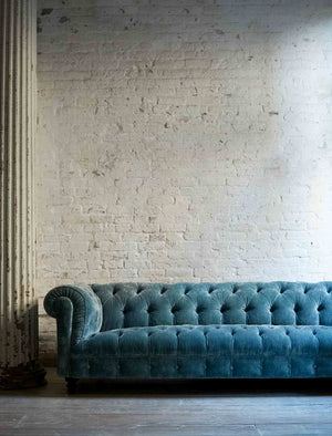  Daytime lighting of the Brook sofa in Velluto Aqua in front of a white brick wall with a white column on the left. Photographed in Velluto Aqua. 