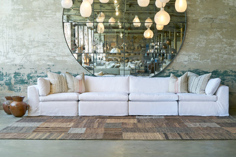 Large white slipcovered modular sofa in front of a large round mirror with white glass lighting pendants. Photographed in Otis White