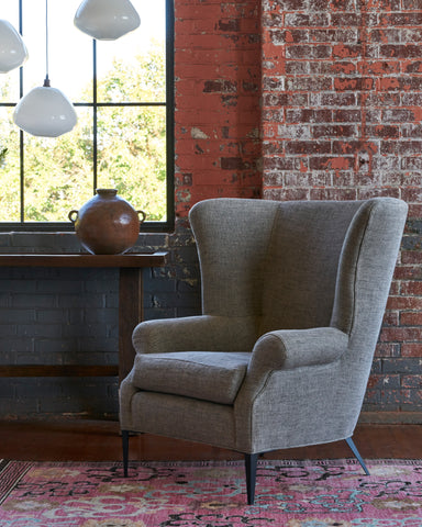 Melrose Chair in Raven Peppercorn in front of a pink and grey brick wall with a wood console and a pot