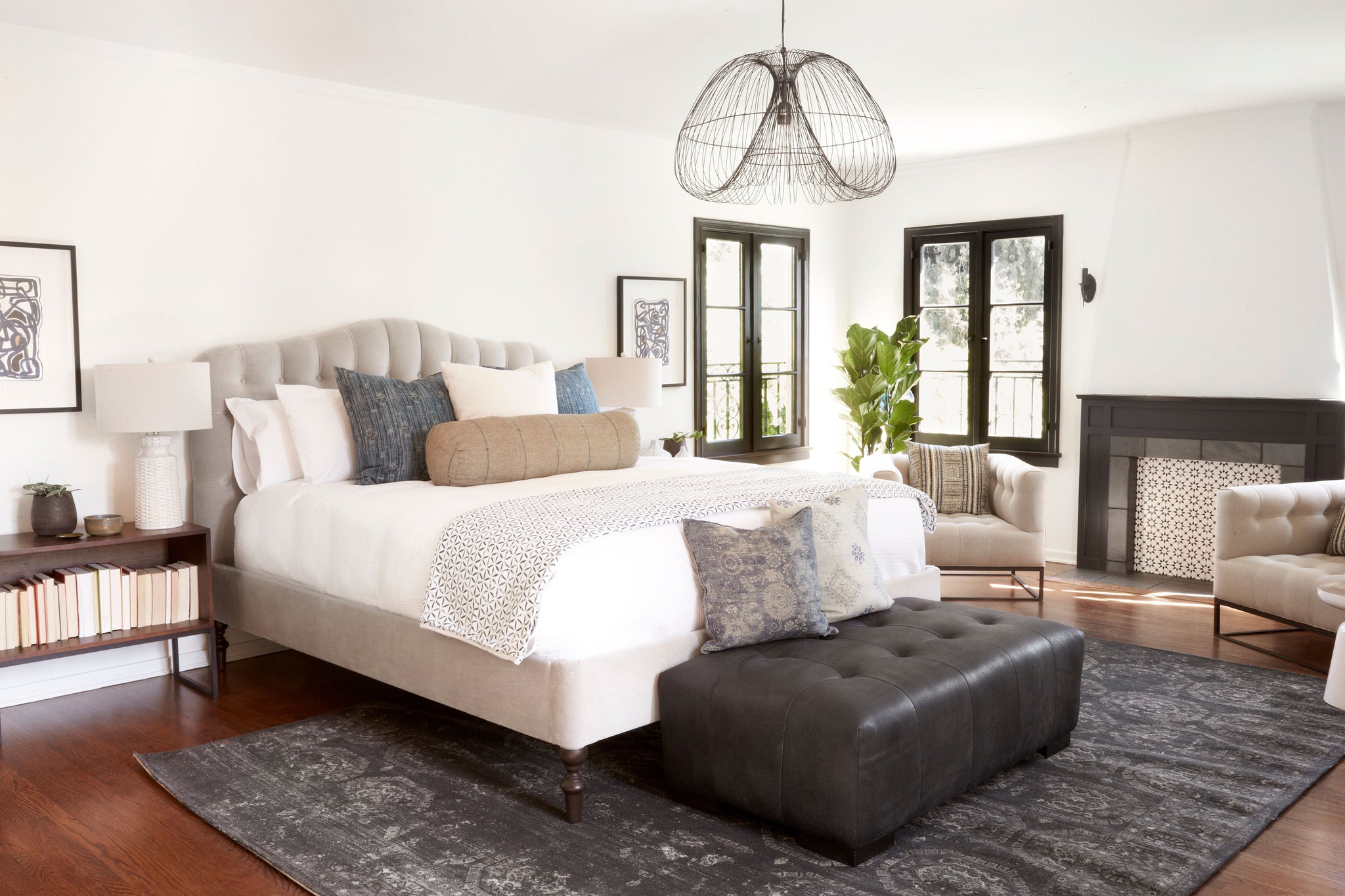  O'hara bed in Matteo Stone next to two chairs and an ottoman at the end of the bed. In the background is a white room with two windows. Above the room hangs a chandelier. Photographed in Mateo Stone. 