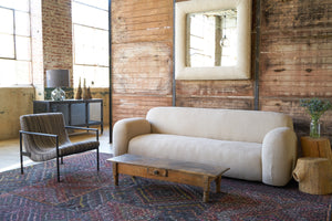  Sofa side view with a chair on the left and a wood table in front.  Photographed in Brevard Burlap. 