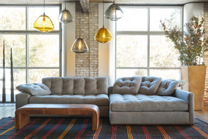  Large brown sectional in front of windows. A leather table is in front and there are 5 glass light pendants above. High terracotta pot with branches on the right. Photographed in Bellamy Pewter. 