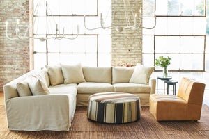  Sunset 2 Arm Sectional in Miles Oatmeal next to a striped ottoman with a white chandelier above. Photographed in Miles Oatmeal. 
