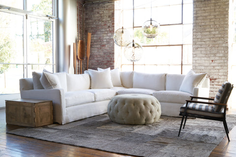 White 2 arm sectional in a showroom with a pouf in the center and a striped chair on the right. Photographed in Brevard Ivory.
