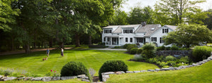 outdoor green field with large traditional farmhouse on the right. Large lush trees surrounding the property