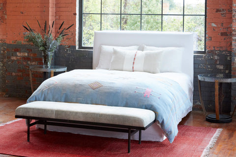 Bedroom with a bed and bench in front of a large window with a red brick wall. Photographed in Logan White.