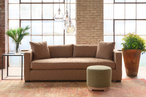 Brown sofa in a room with large windows and decorative plants. Photographed in Lucerne Hazelnut.