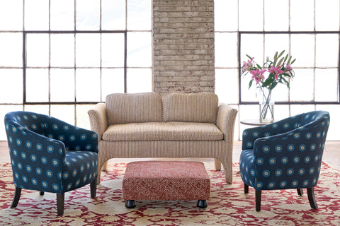 Living room with beige sofa, two blue patterned armchairs, and a red ottoman. Photographed in Florence Sienna.