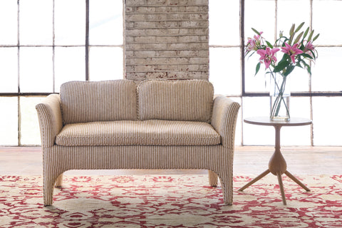Striped loveseat in front of windows with a side table and flowers on top. Photographed in Shiloh Tumeric.
