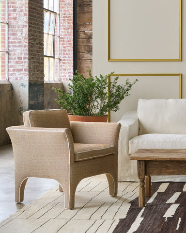 Beige armchair and white sofa in a room with brick wall and large windows. Photographed in Reed Gold.