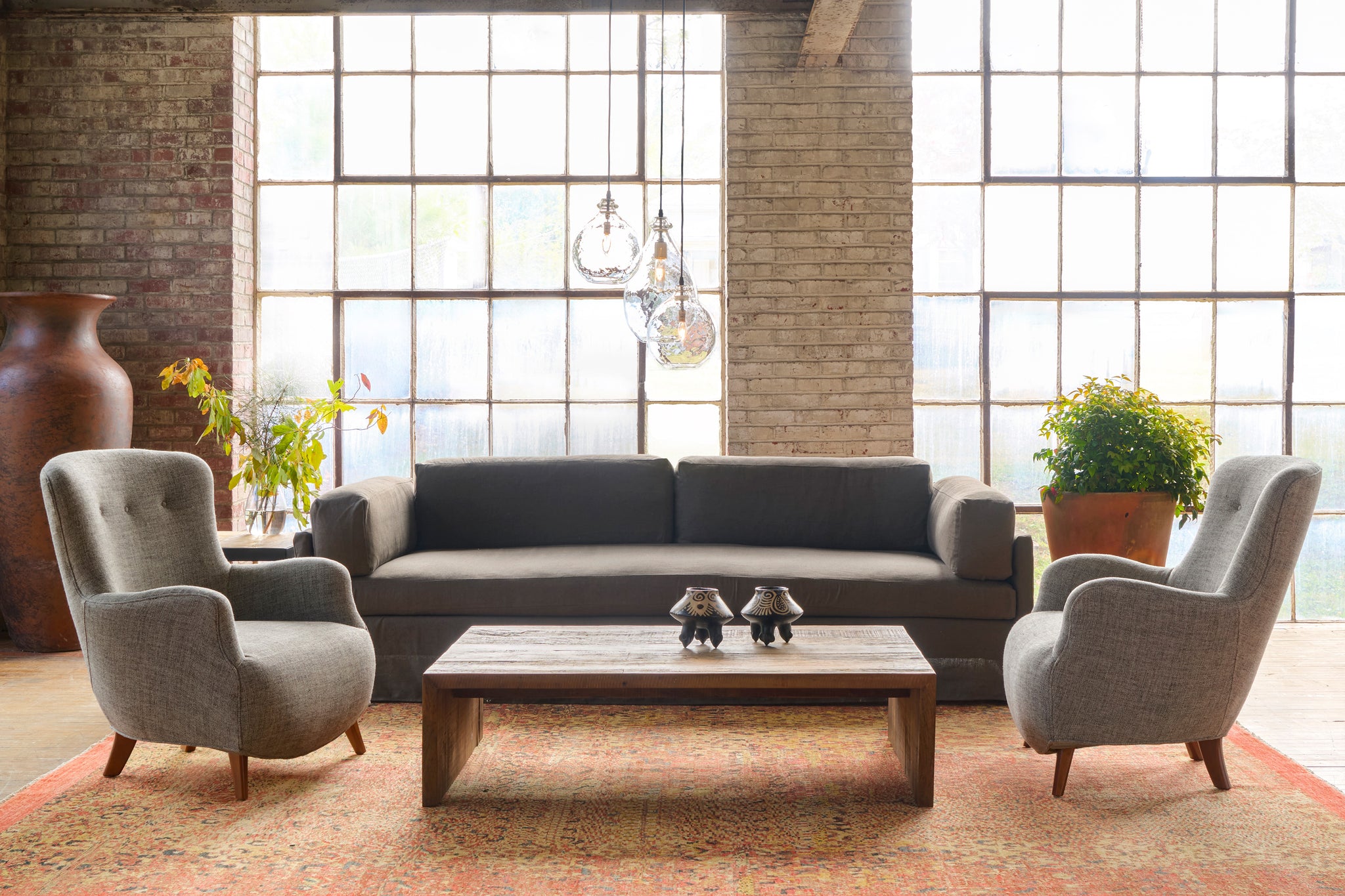  Modern living room with a dark brown sofa, armchairs, and coffee table in front of large windows. Photographed in Miles Walnut. 