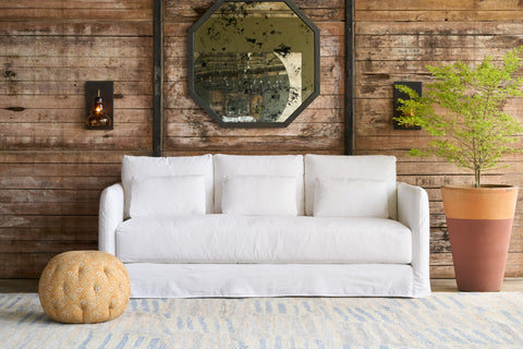 White sofa in a room with wooden walls, a mirror, and a plant. Photographed in Mia White.