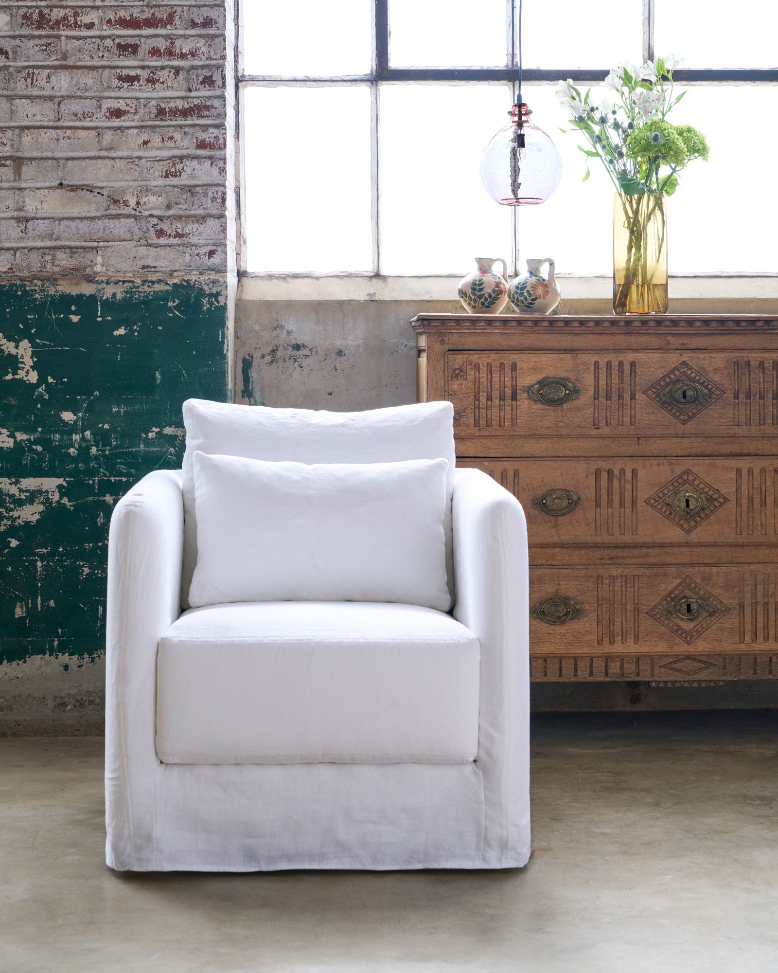  White slipcovered chair in front of a chest of drawers. Photographed in Otis White. 