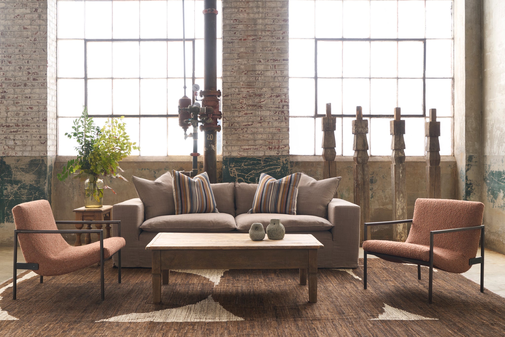  Brown sofa in a showroom with 2 chairs on a brown rug with 4 wood pillars on the right and flowers on the left. Photographed in Rye Acorn. 