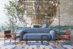  Grey sofa in front of an oversized mirror with two metal and leather chairs on each side. Metal pendants and metal floor lamp on the right. 