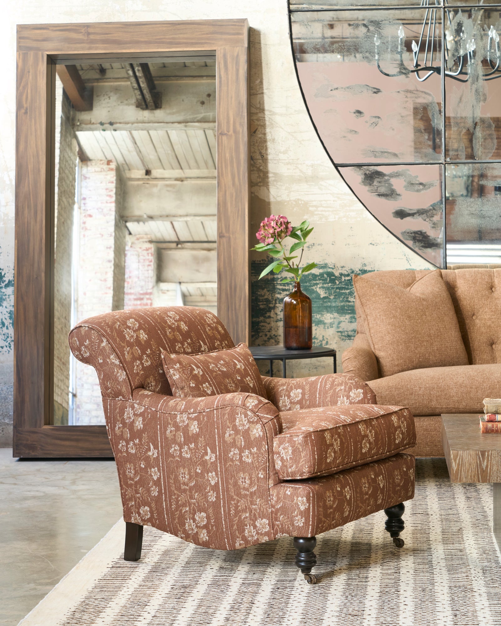 Patterned armchair in a living room with a large mirror and floral arrangement. Photographed in Foret Rust. 
