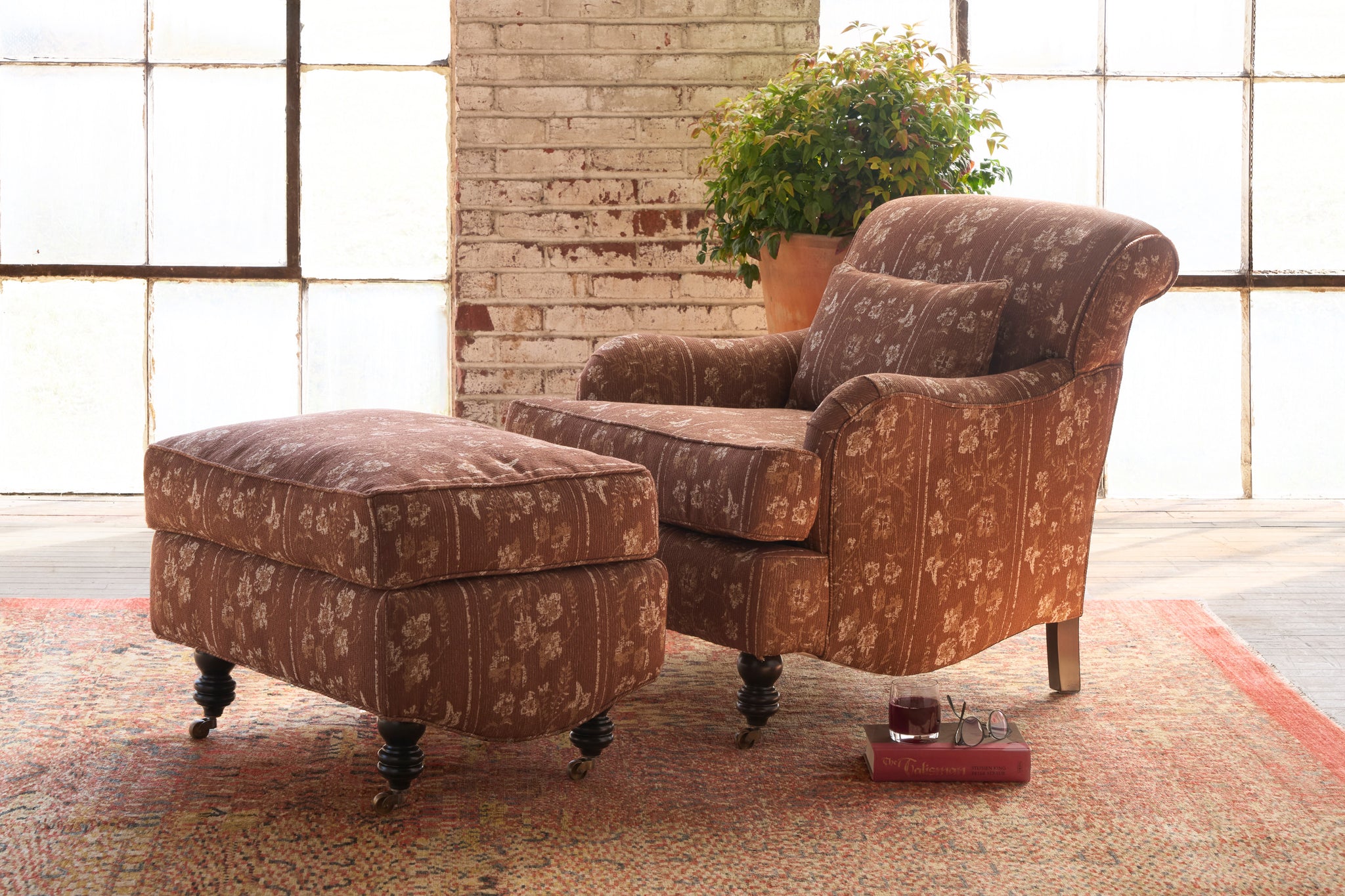  Brown patterned armchair and ottoman in a room with large windows and a brick wall. Photographed in Foret Rust. 