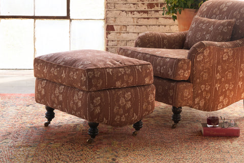 Brown patterned armchair and ottoman on a textured rug with a brick wall background. Photographed in Foret Rust.