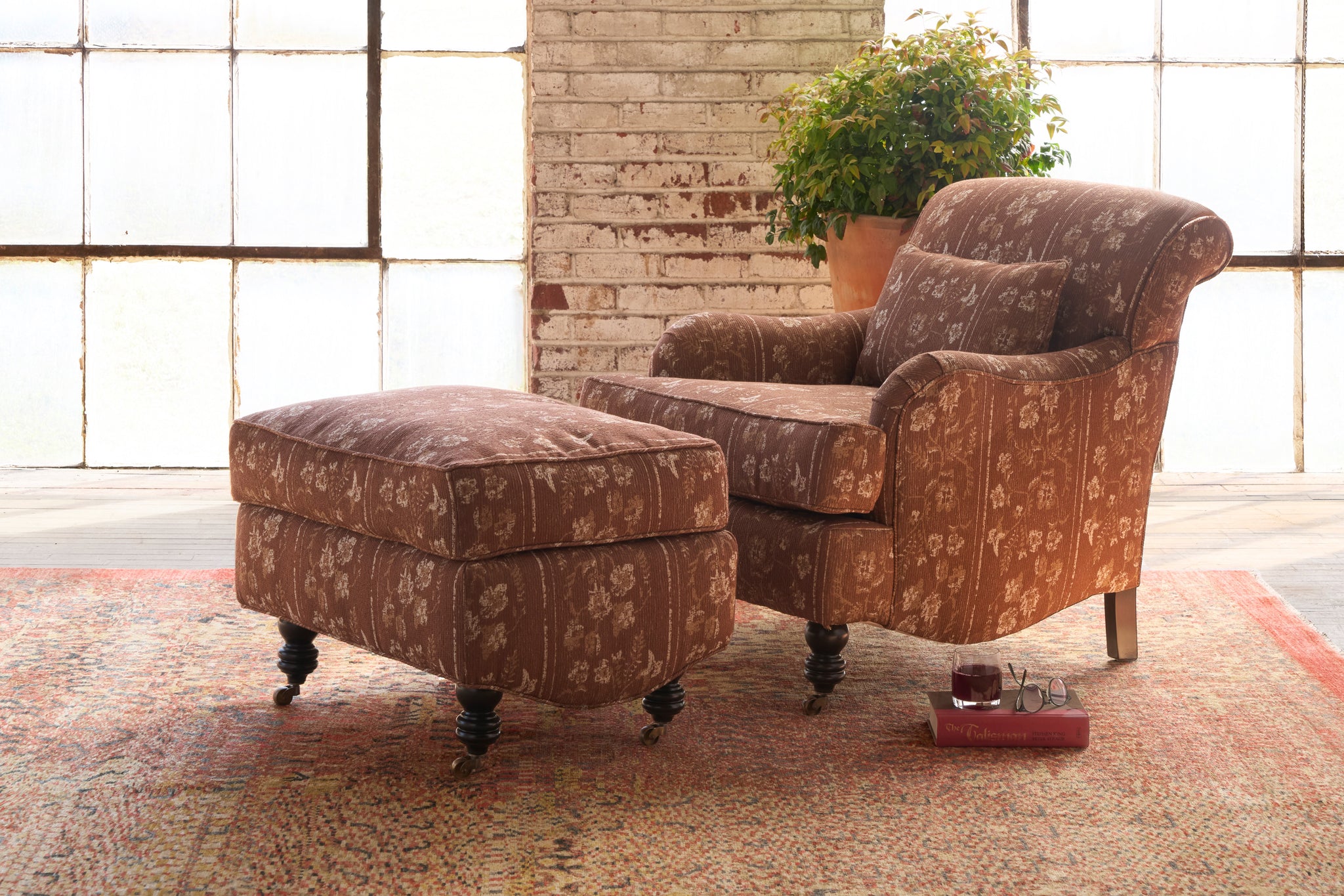  Brown patterned armchair and ottoman with a plant in the background. Photographed in Foret Rust. 