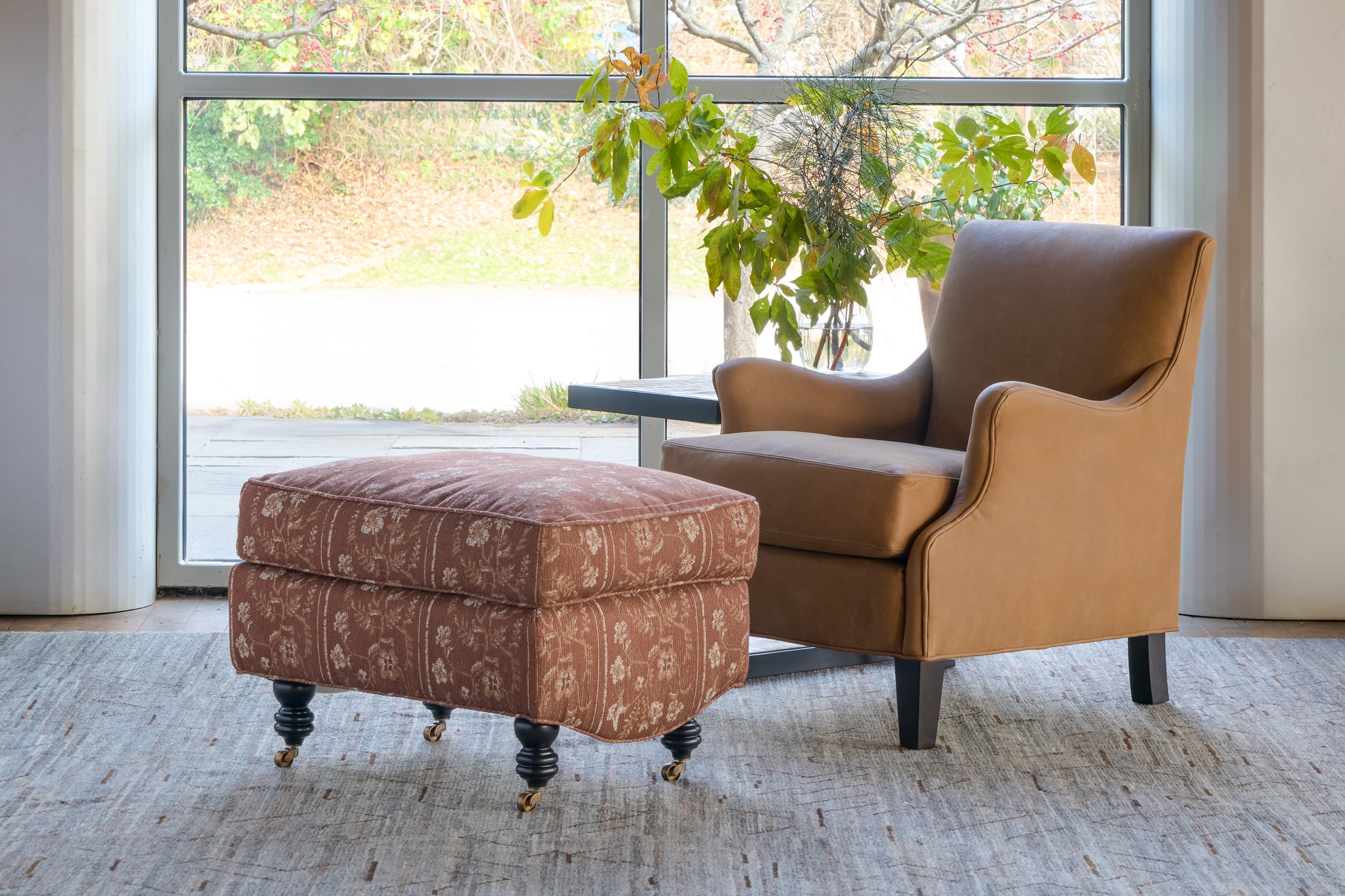  Brown armchair and ottoman in a room with large windows and plants. Photographed in Foret Rust. 