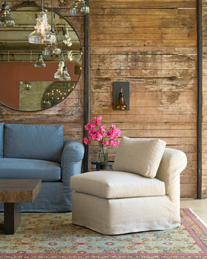  Oatmeal chair with a rolled back in front of a wood wall next to a blue sofa. Photographed in Devon Oatmeal. 