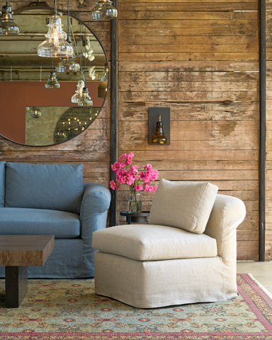 Oatmeal chair with a rolled back in front of a wood wall next to a blue sofa. Photographed in Devon Oatmeal.