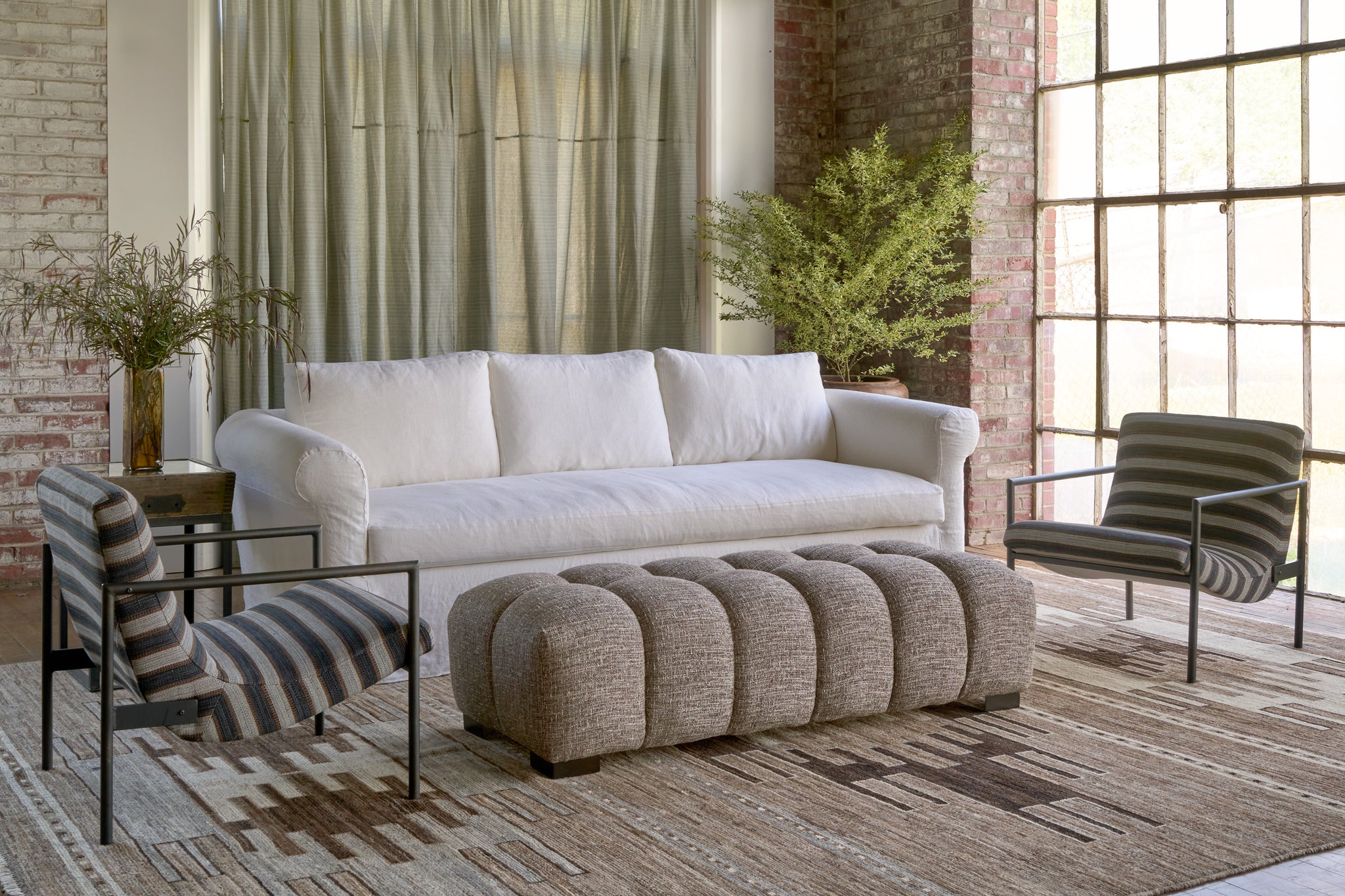  White sofa with a brown bench in front and 2 striped chairs on the side. Photographed in Rayas Noire. 