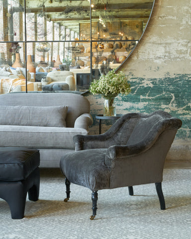 Grey velvet chair in front of a sofa and a large mirror on the wall. Photographed in Velluto Slate.
