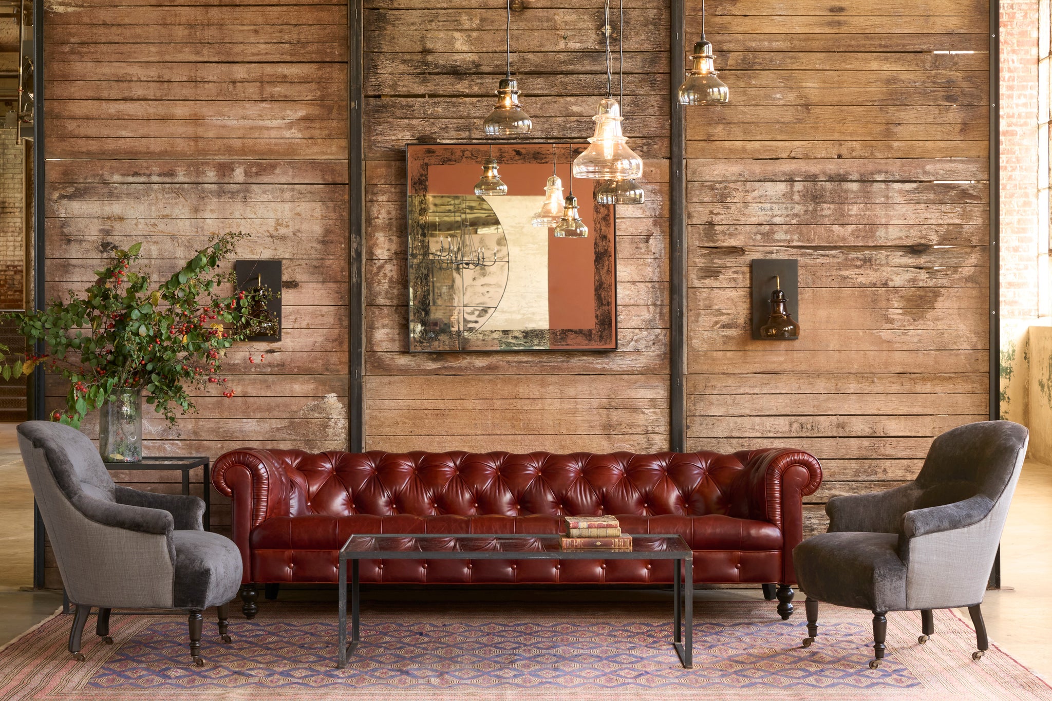  Red leather sofa with gray armchairs in a room with wooden walls and hanging lights. Photographed in Velluto Slate and Rye Warm Grey. 