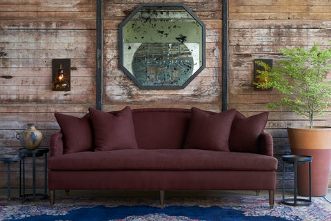 Burgundy sofa in front of a wood wall with a mirror. Photographed in Devon Merlot.