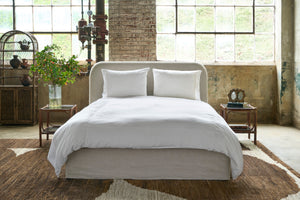  Bed in a showroom with big windows on a brown rug. Photographed in Devon Oatmeal. 