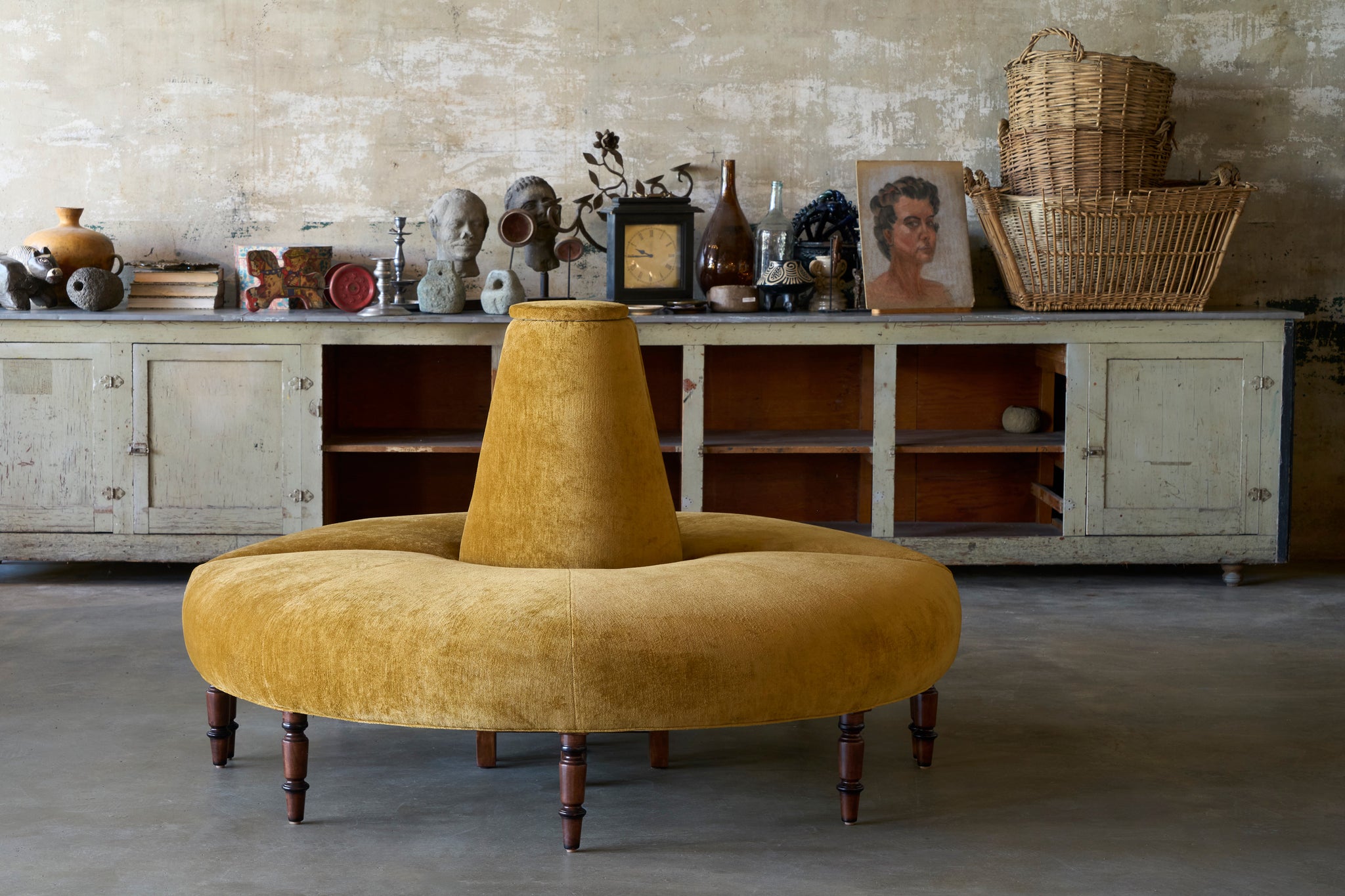  Mustard yellow circular ottoman with wooden legs in a room with a rustic decor. 