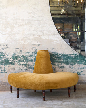  A gold velvet round sofa in front of a wall with a mirror. Photographed in Velluto Gold. 