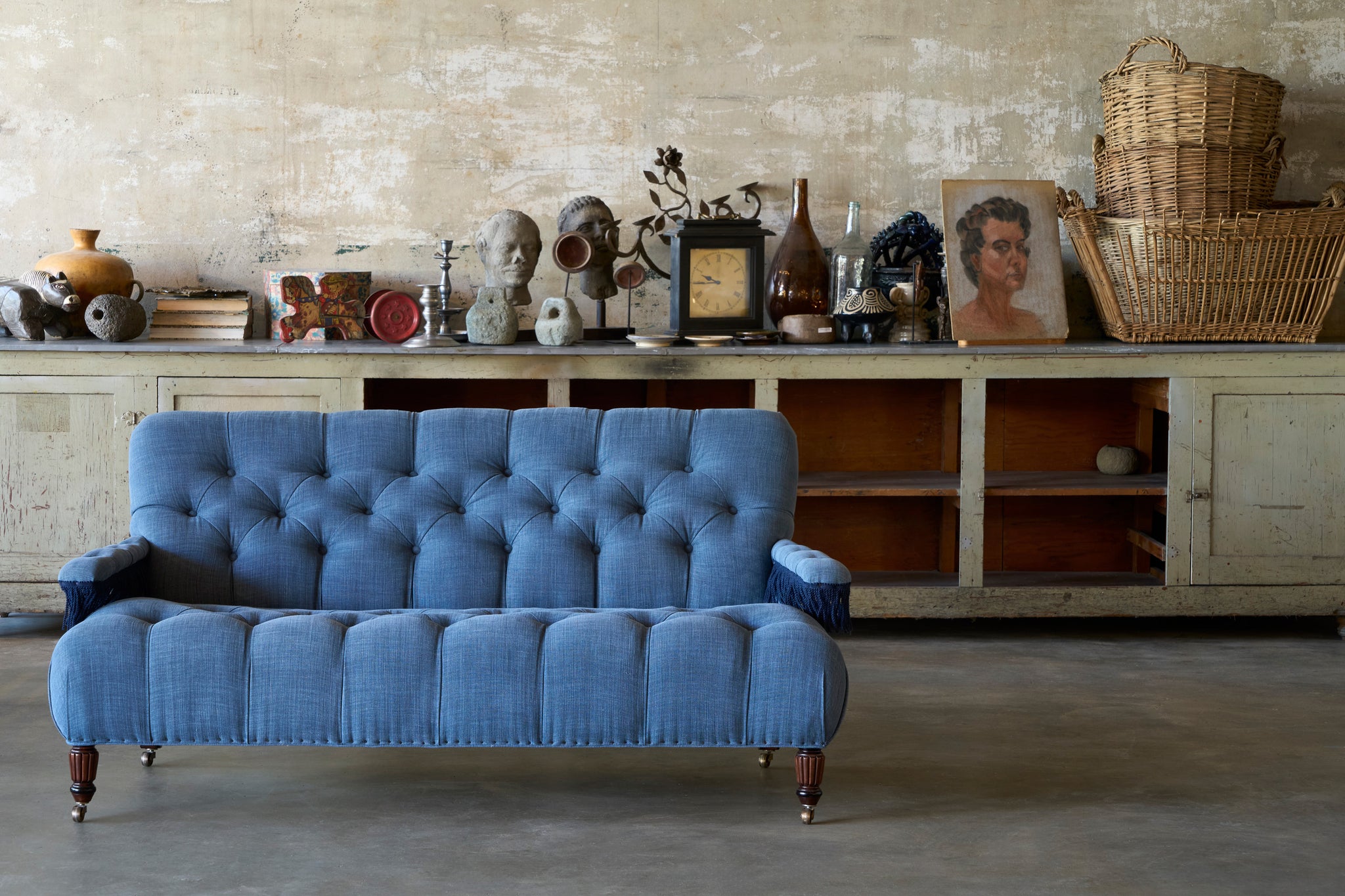  A blue tufted sofa in front of a console with various vintage pieces on top. Photographed in Rye Midnight Blue. 
