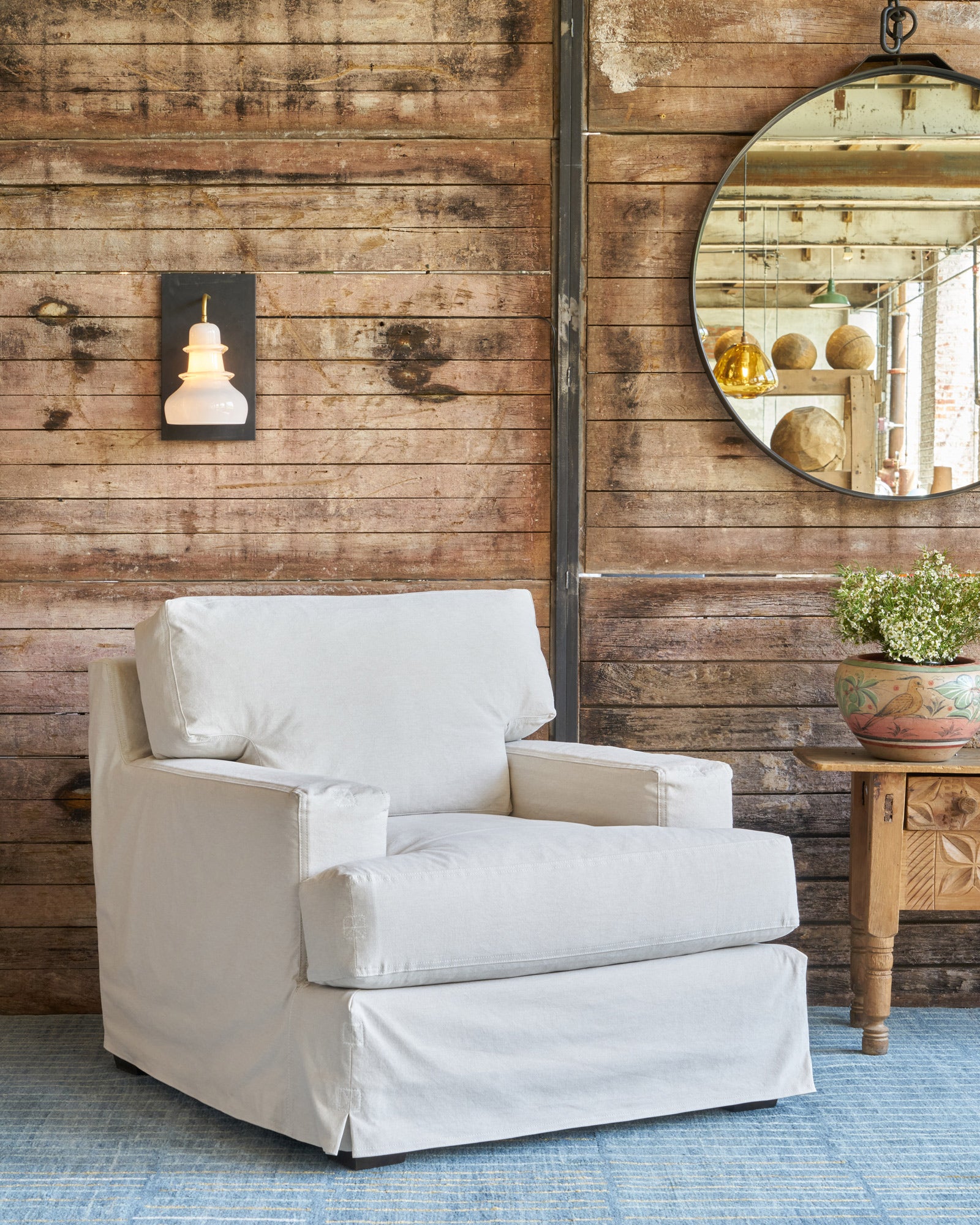  Armchair in front of a wood wall. White glass sconce and round mirror behind. Photographed in Luna Oatmeal. 