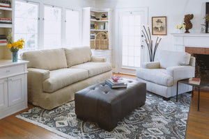  Living room with sofa and armchair and a leather tufted bench in the center. Photographed in Indiana Charcoal. 