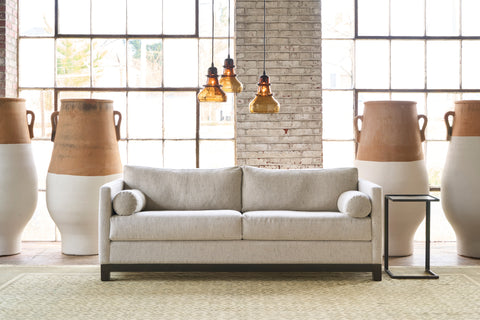 Oatmeal colored sofa in front of windows with 4 pots. There are 3 brown glass pendants. Photographed in Andrews Natural.