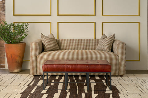 Living room with a checkered sofa, red leather ottoman, and framed artwork on the wall. Photographed in Georgie Cinnamon.