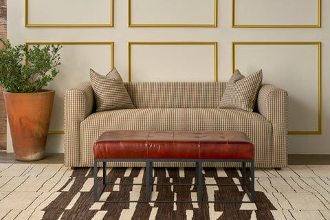 Sofa in front of a wall with molding and a planter. A leather ottoman in front. Photographed in Solvang Chianti.