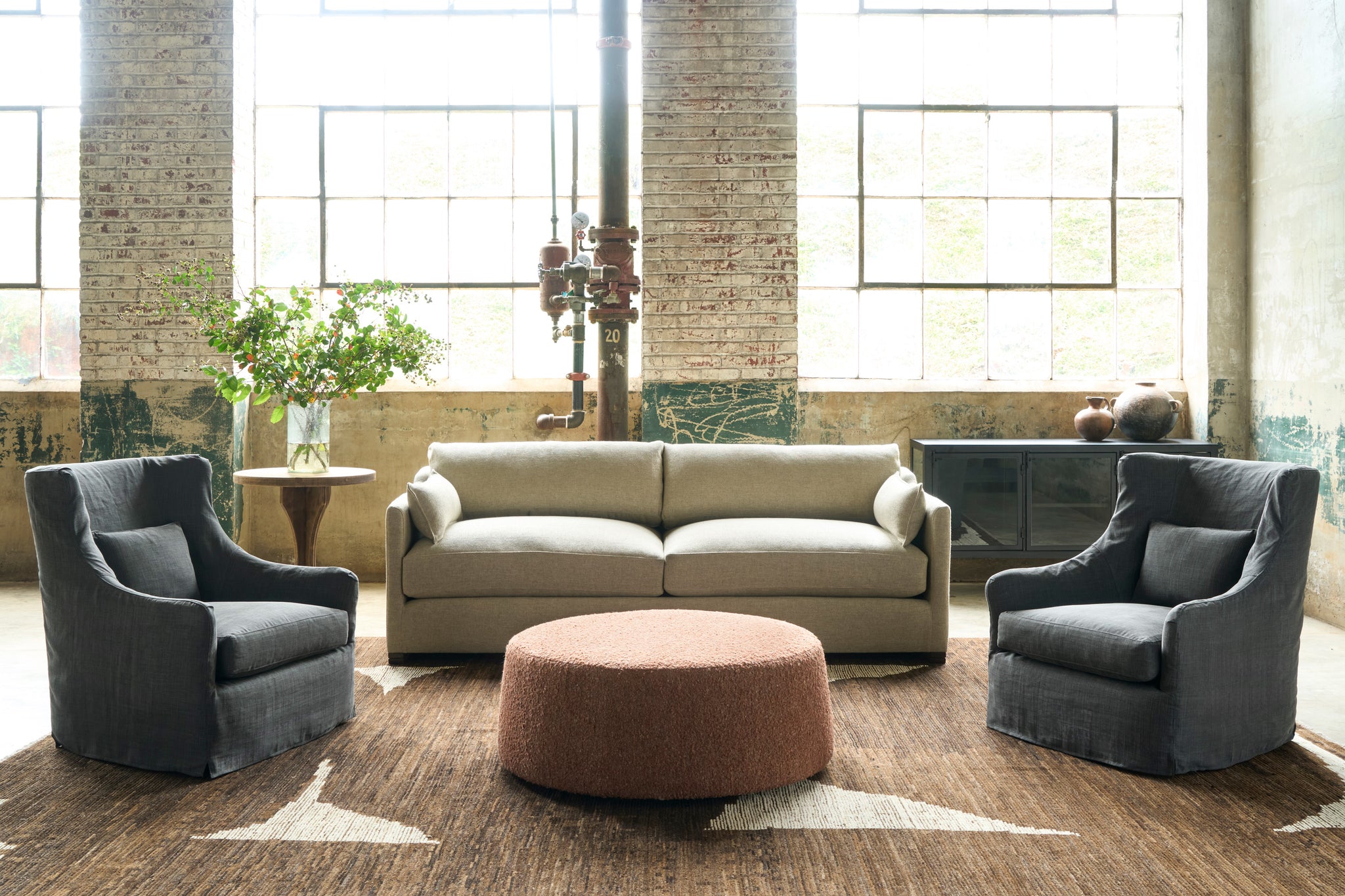  Oatmeal colored sofa with 2 dark grey wing chairs and an orange ottoman on a brown and white rug. Photographed in Bellamy Natural. 