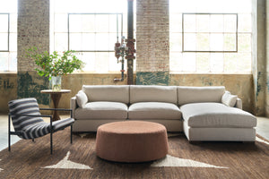  Sectional in a showroom with a striped chair on the left and an orange ottoman in front. Photographed in Bellamy Natural. 