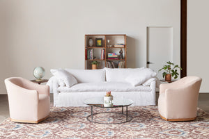  White sofa with 2 pink chairs on a brown and blue rug. A bookcase is in the background. A mirror top round coffee table is in the middle. Photographed in Logan White. 