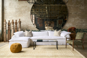  White sectional in front of a large mirror. Five wood sculptures on the left and a red plant on the right.
Metal coffee table in the middle. Gold velvertpouf in front and green chair with wood frame of the right. Photographed in Logan White. 