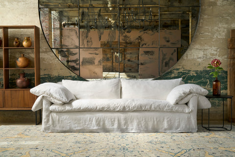 White sofa in a room with a large decorative mirror and wooden shelf. Photographed in Logan White.